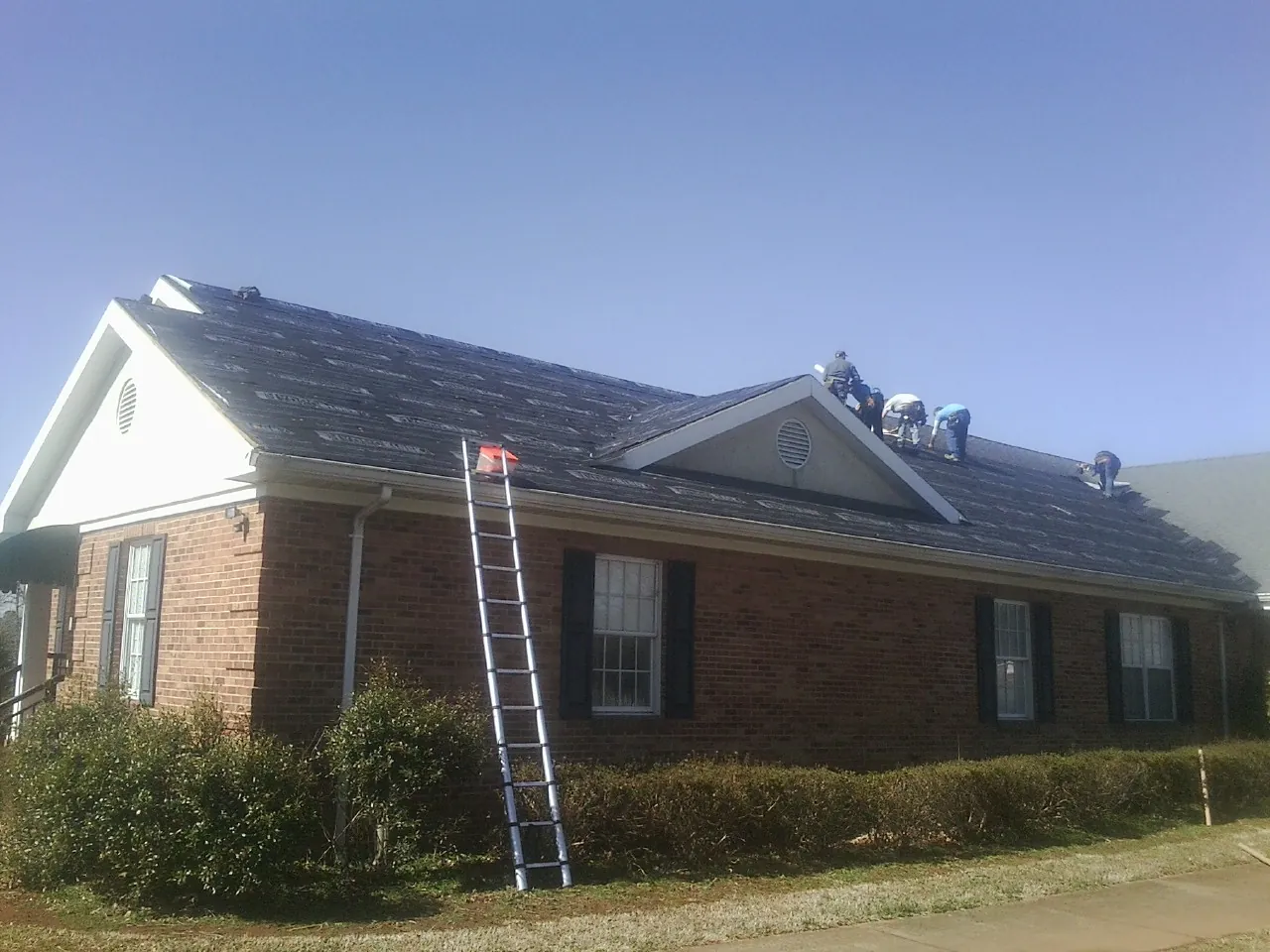Crew tearing shingles off a brick ranch roof with a ladder set — Emergency Roof Repair work by our crew in Hammond