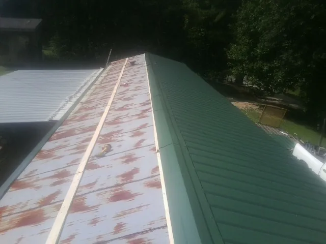 Old rusted panels beside newly installed green metal roofing — Wind Damage Roof Repair by Roofing Brothers in Hammond