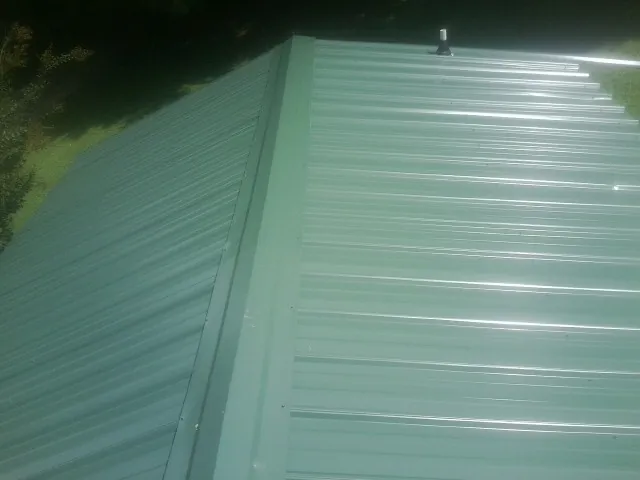 New green metal panels meeting at the ridge of a roof — Flat Roof Repair work by our crew in Hammond
